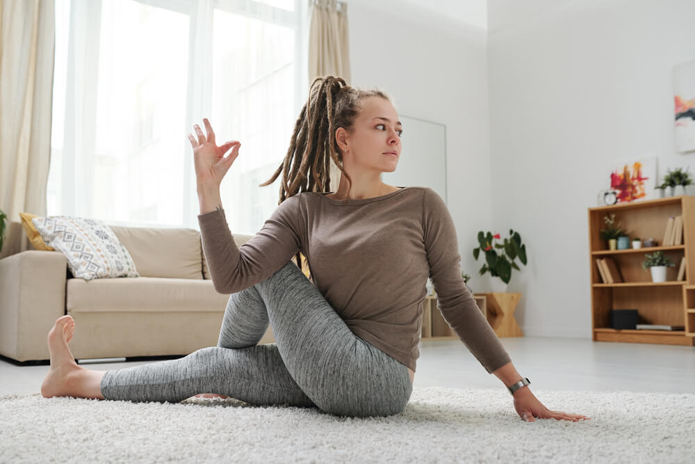 Young female with dreadlocks sitting on the floor in one of yoga posit